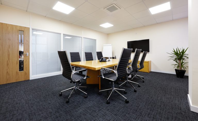 wooden boardroom table with black chairs and TV mounted on wall