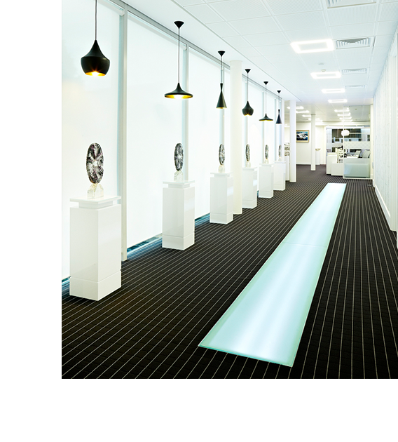 long wide corridor with stripy carpet, black pendant lights, illumintae section of floor and plinths eith trophies on