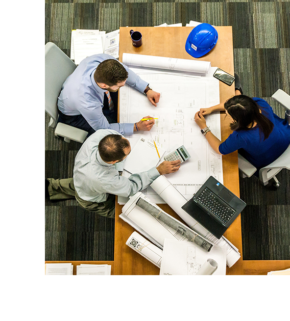 3 people sitting around a desk looking at plans