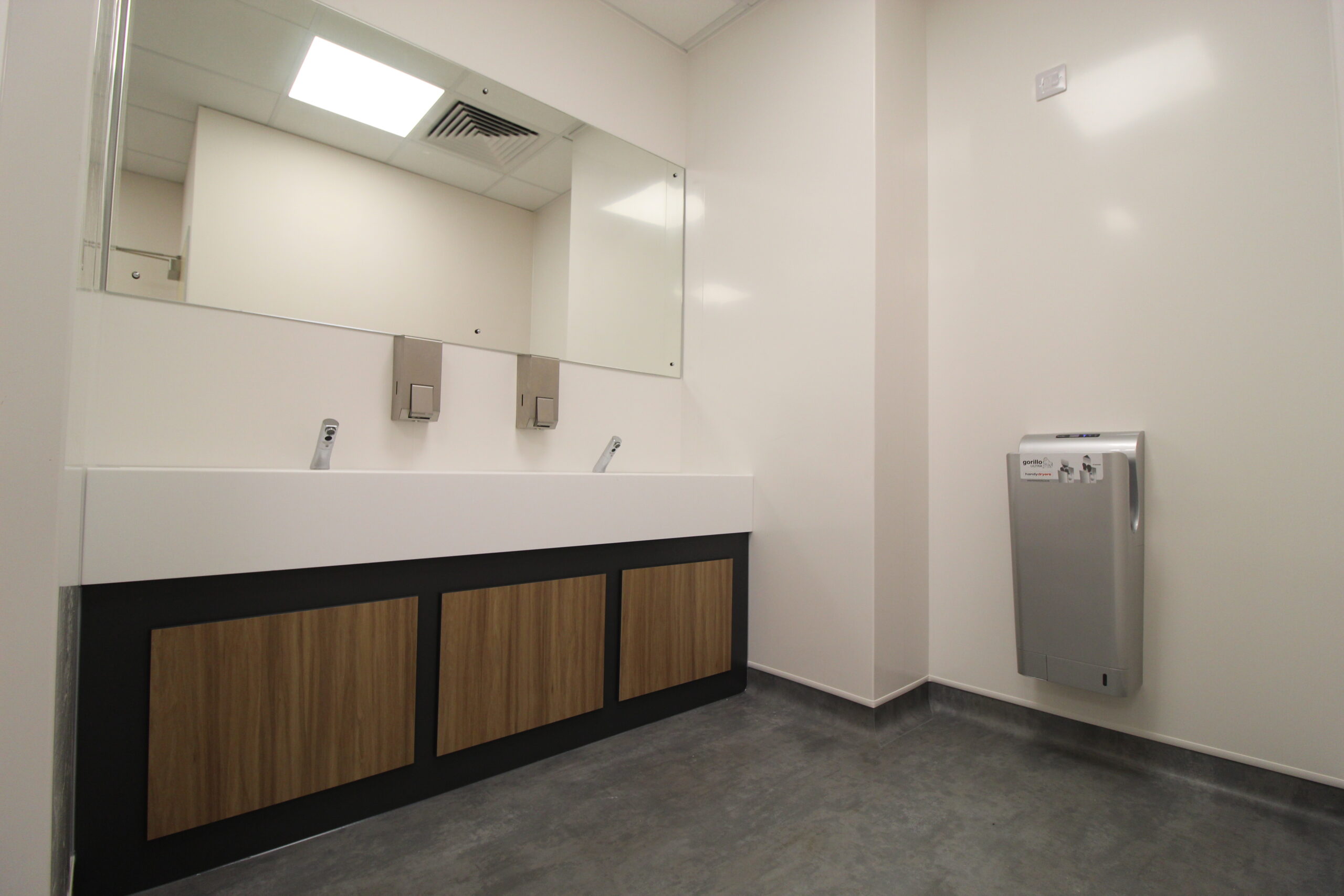 Washroom with mirror on wall, stainless steel taps and hand drier.