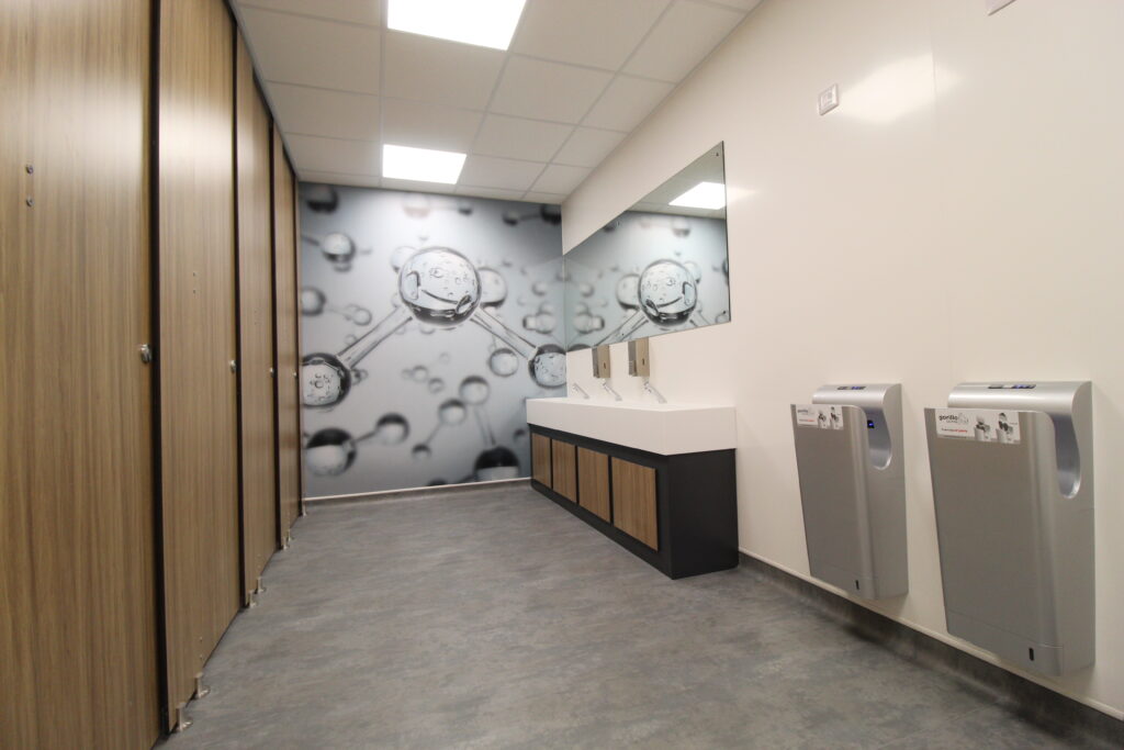 Washroom with cubicles and hand driers. Wall graphic at rear end of room.