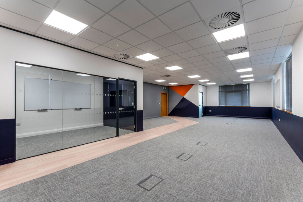 open plan office space with gray carpet, glass partitioning and painted feature wall