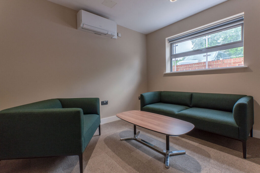 Small wellbeing meeting room with green sofas and natural timber table of metal legs