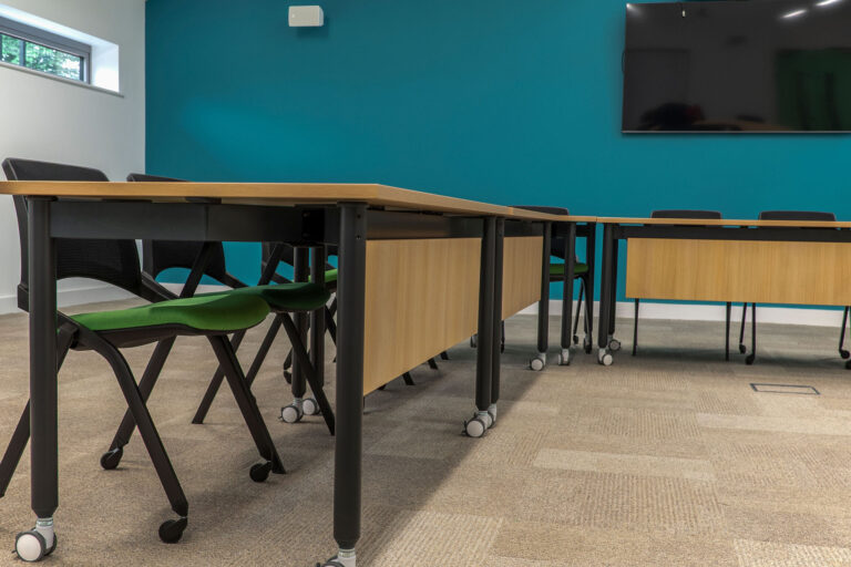 Close up image of rectangle desks with green padded chairs on castors