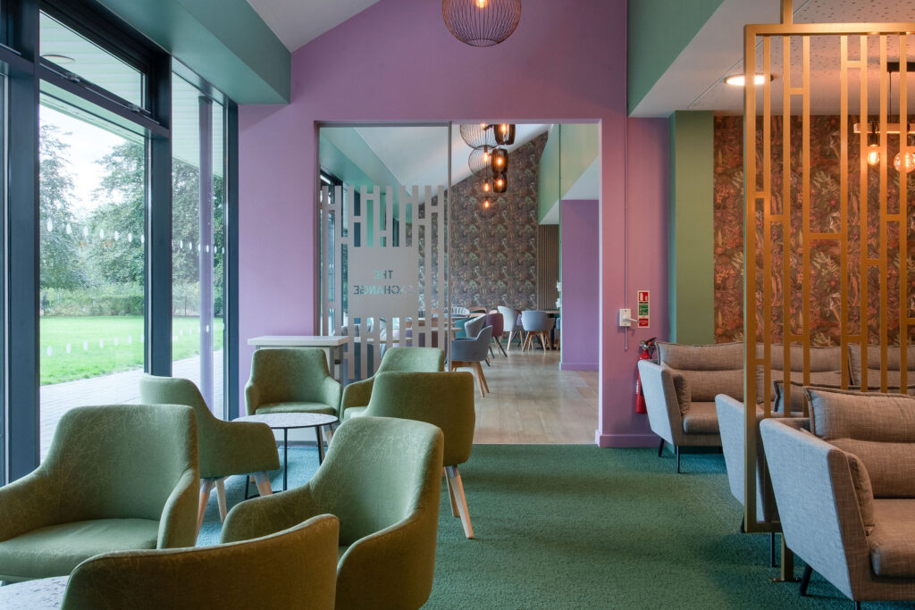 Wall paper and pink feature wall in bacground, with coffee tables and green chairs