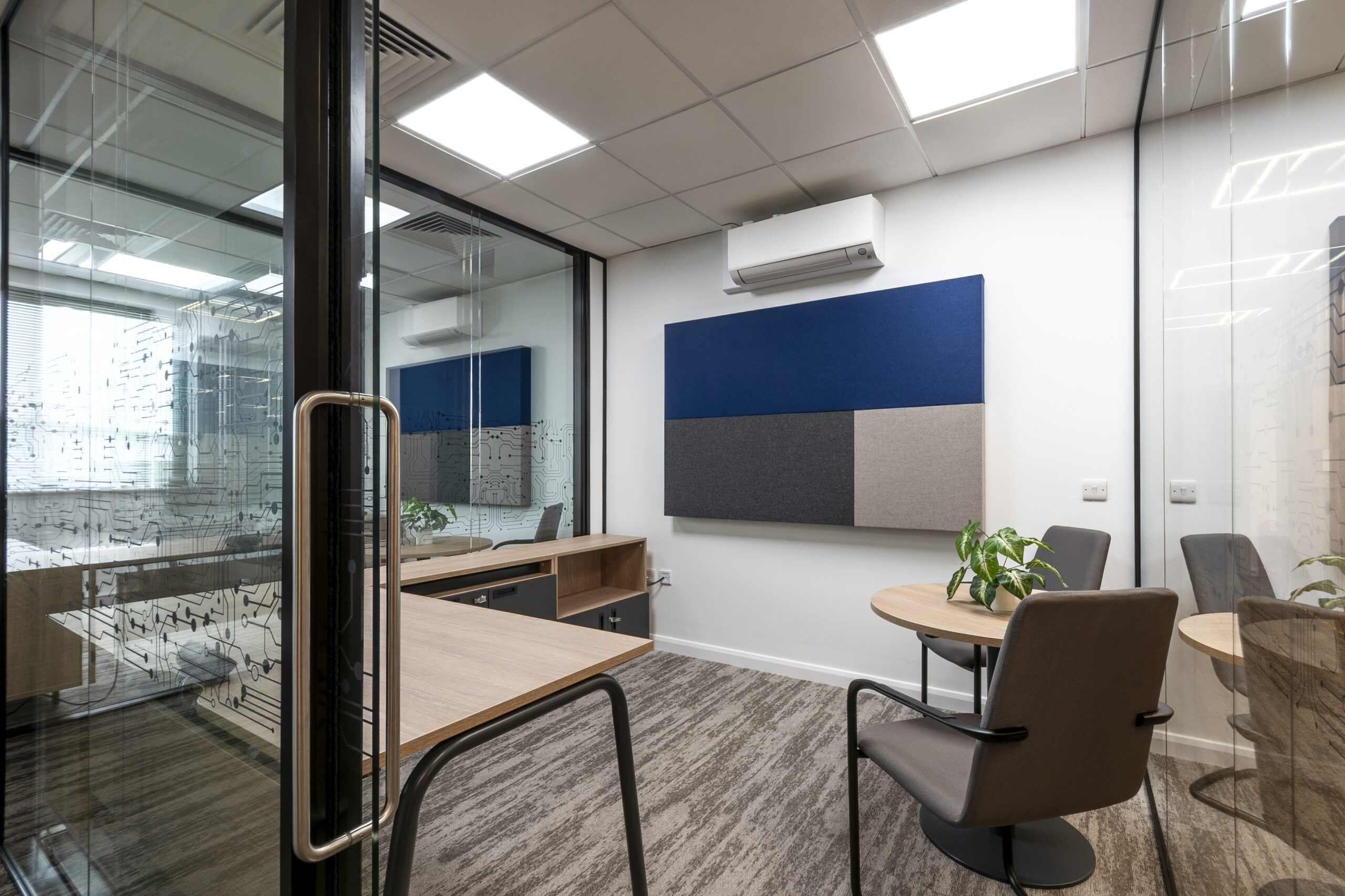 Corner office with grey seating and carpet, acoustic wall panel and glass partitioning